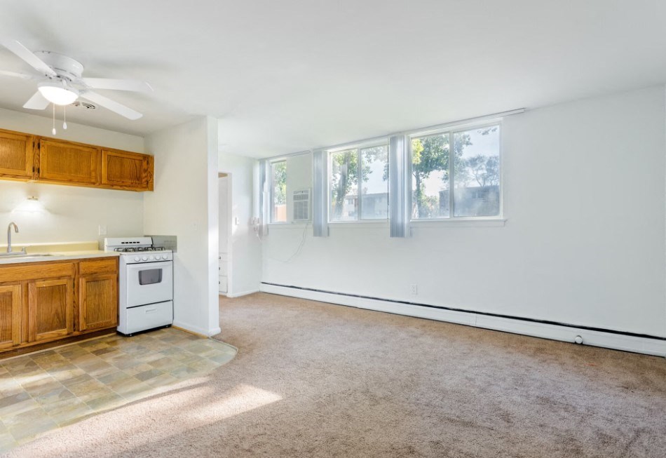 an empty living room with a kitchen and a ceiling fan